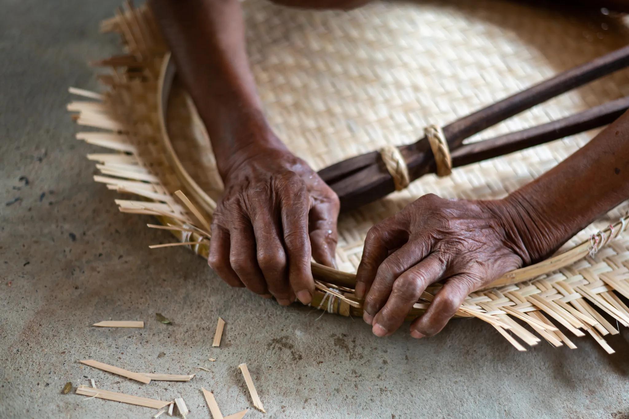 Close up Old man Hand weaving wicker basket or bamboo basketry indoors Weaving bamboo fish trap in Thailand closeup view Photo credit Thammanoon Khamchalee via Shutterstock
