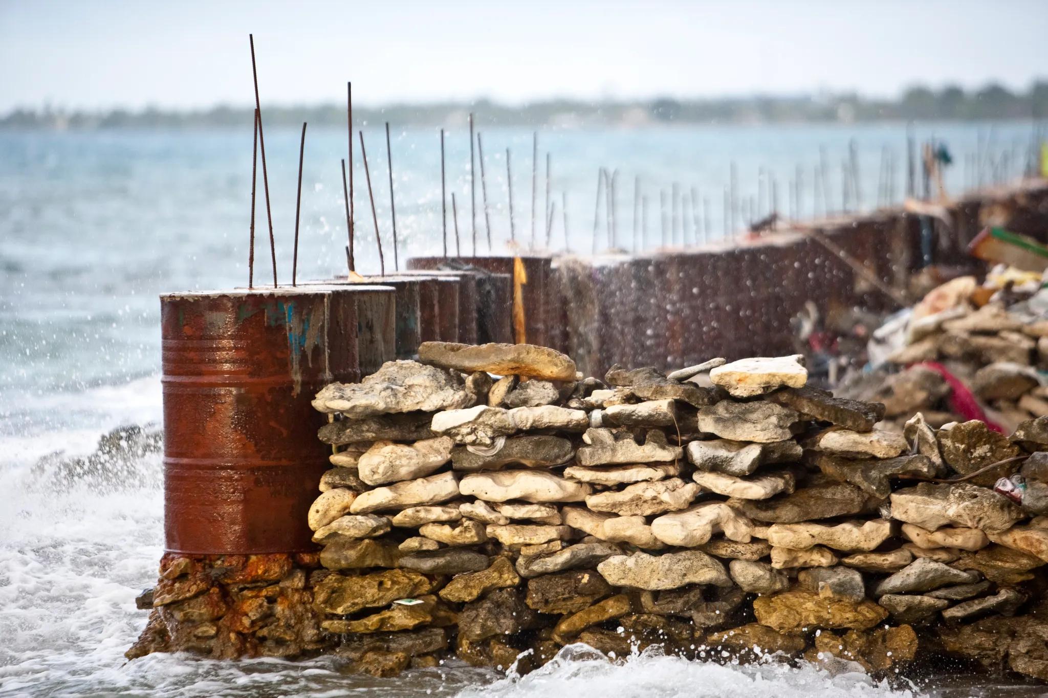Fuel drums in a row with sandbags being used to make a sea defence wall/ Credit: Rodney Dekker via Climate Visuals